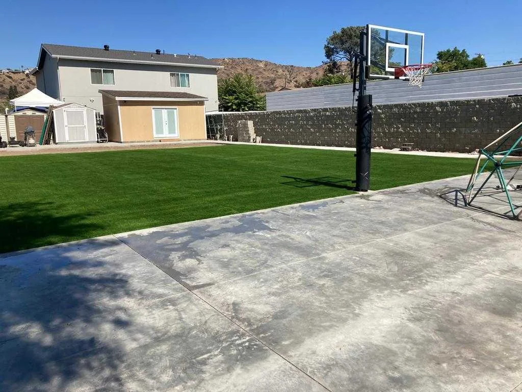Large backyard with installed artificial grass and a basketball hoop